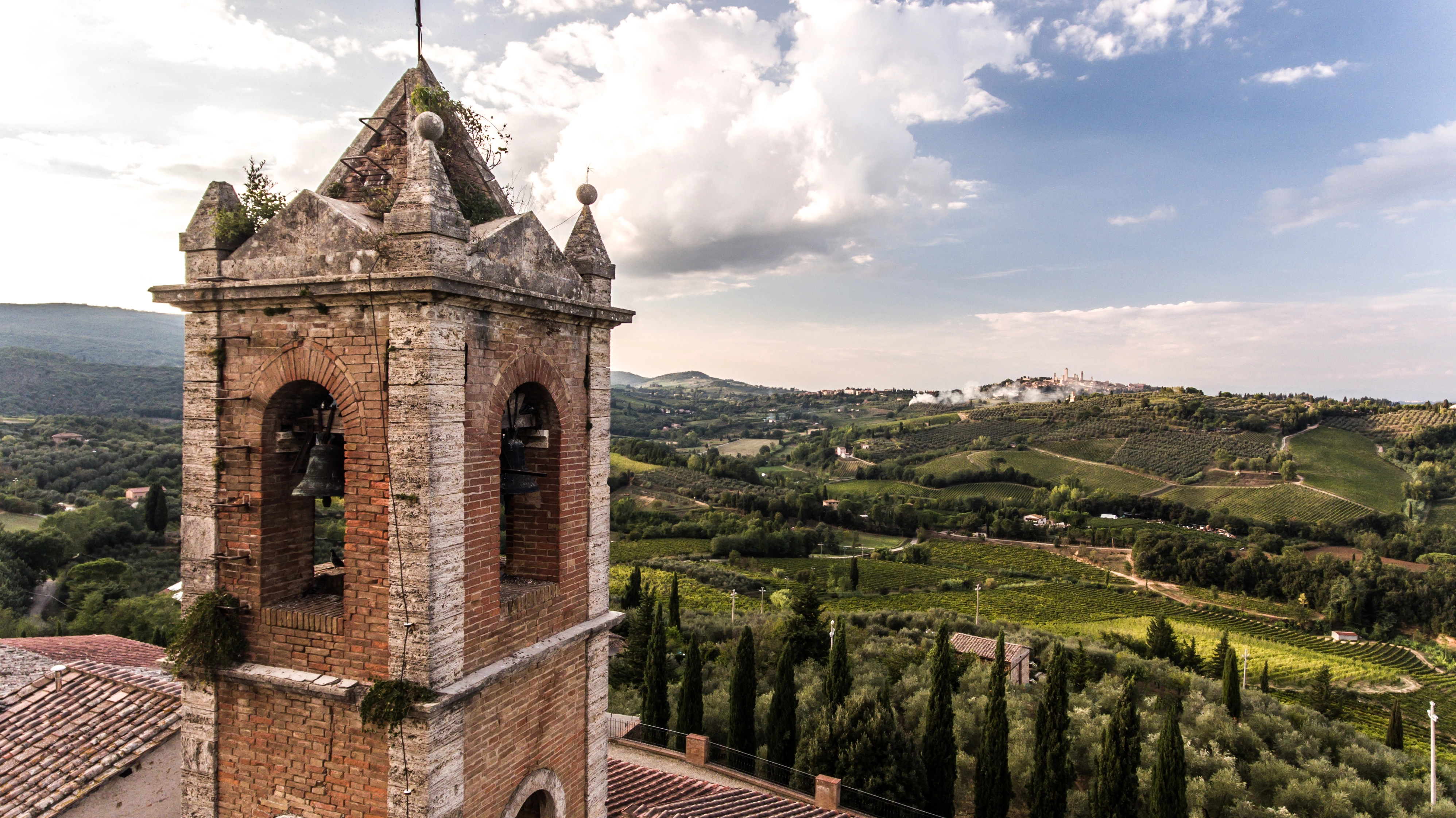 Landschaftsaufnahme des Weinguts der Famiglia Cecchi in der Toskana mit Kirchturm im Hintergrund, umgeben von Hügeln und Natur