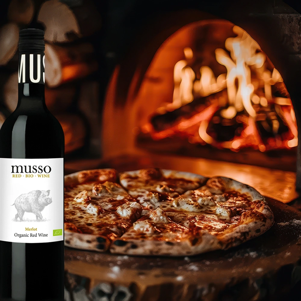 Musso Merlot Bio Rotwein mit rustikaler Pizza vor einem Holzofen mit offenem Feuer