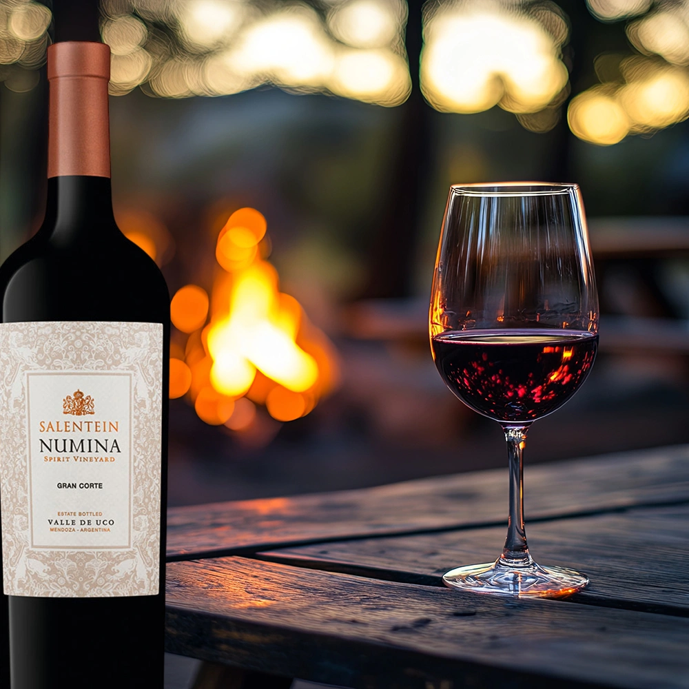 Bodegas Salentein Numina Gran Corte auf einem rustikalen Tisch am Lagerfeuer in stimmungsvoller, abendlicher Outdoor-Atmosphäre