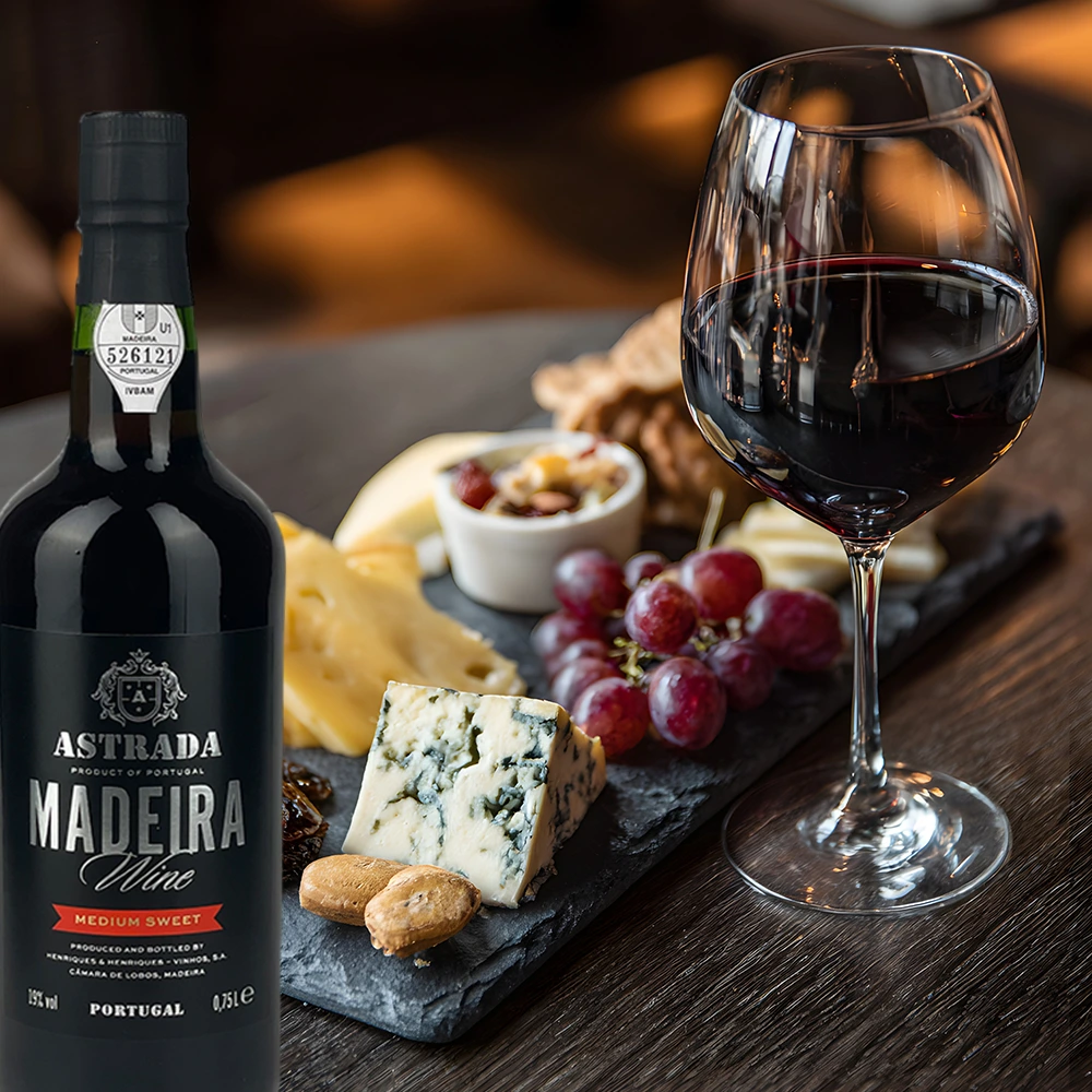 Flasche Astrada Madeira Wein neben einer reichhaltigen Käseplatte auf einem rustikalen Holztisch angerichtet
