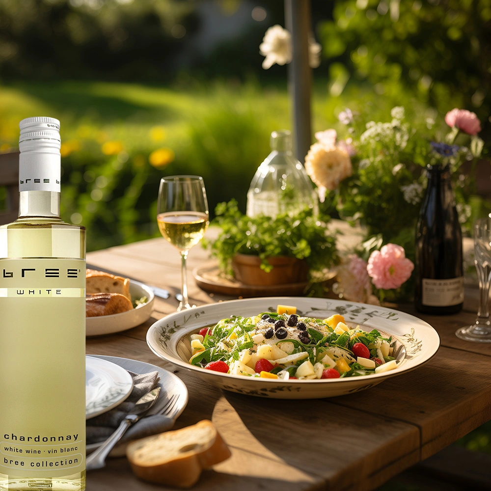 Kleine 0,25-Liter-Flasche Bree Chardonnay auf einem gedeckten Tisch mit einem frischen sommerlichen Salat in einem idyllischen Garten als leichte und elegante Weinbegleitung