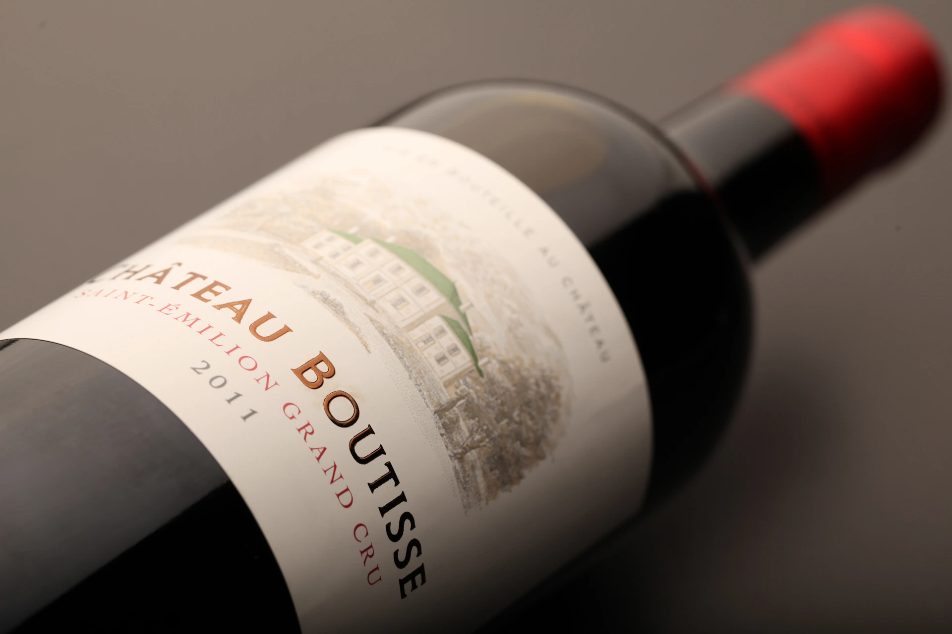 Liegende Flasche Château Boutisse vor grauem Hintergrund mit Etikett in Detailaufnahme
