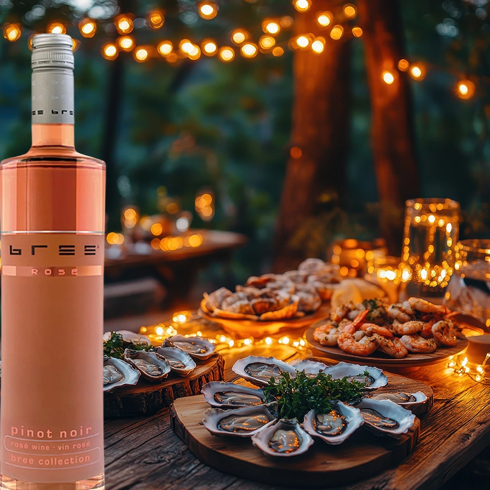 Bree Pinot Noir Rosé Weinflasche auf einem stimmungsvoll gedeckten Abendtisch mit frischen Muscheln, Meeresfrüchten und warm leuchtenden Lichterketten als sommerliche Weinbegleitung