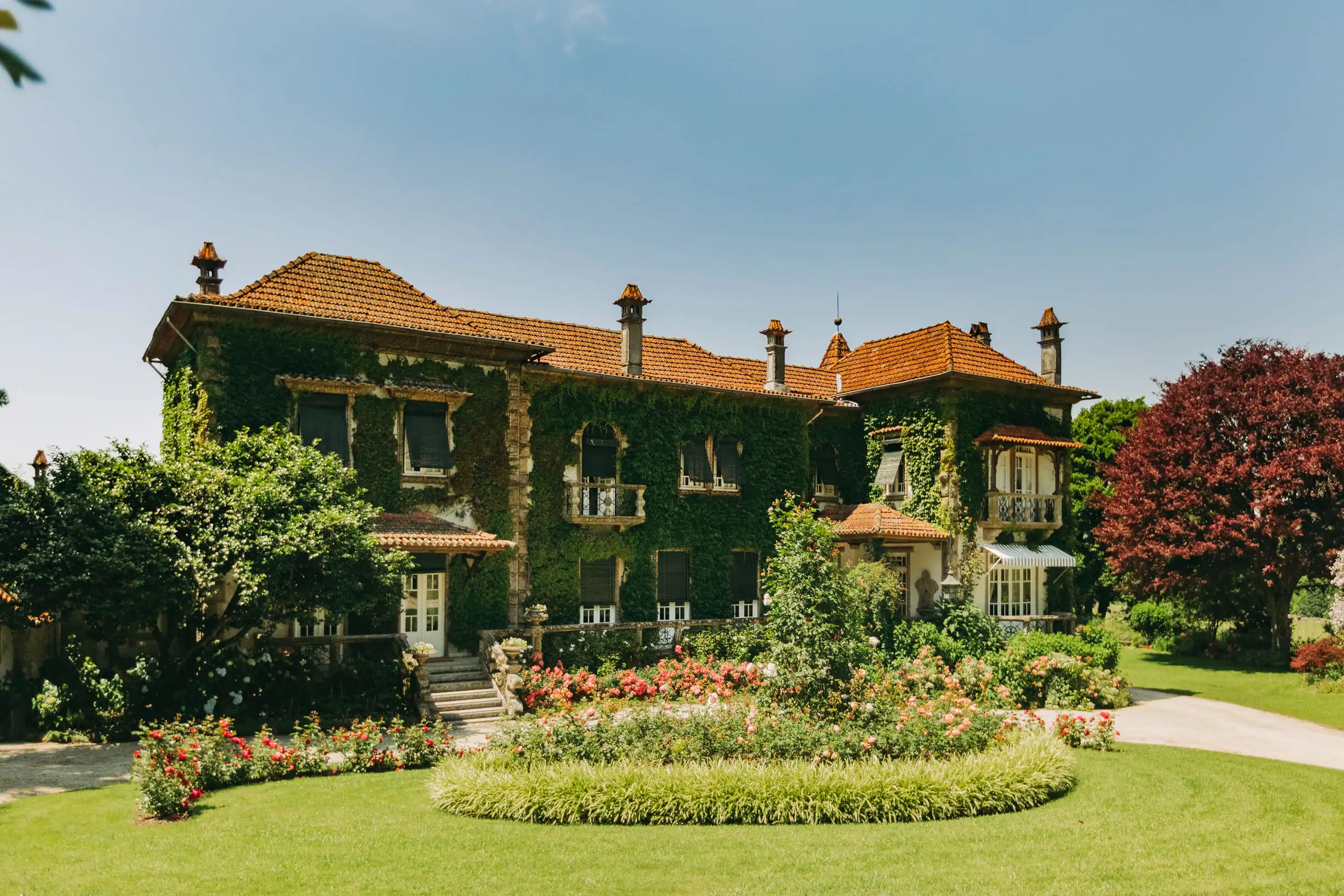 Hauptgebäude des Weinguts Aveleda mit prachtvoll bewachsenem Garten unter blauem Himmel in sonniger Atmosphäre