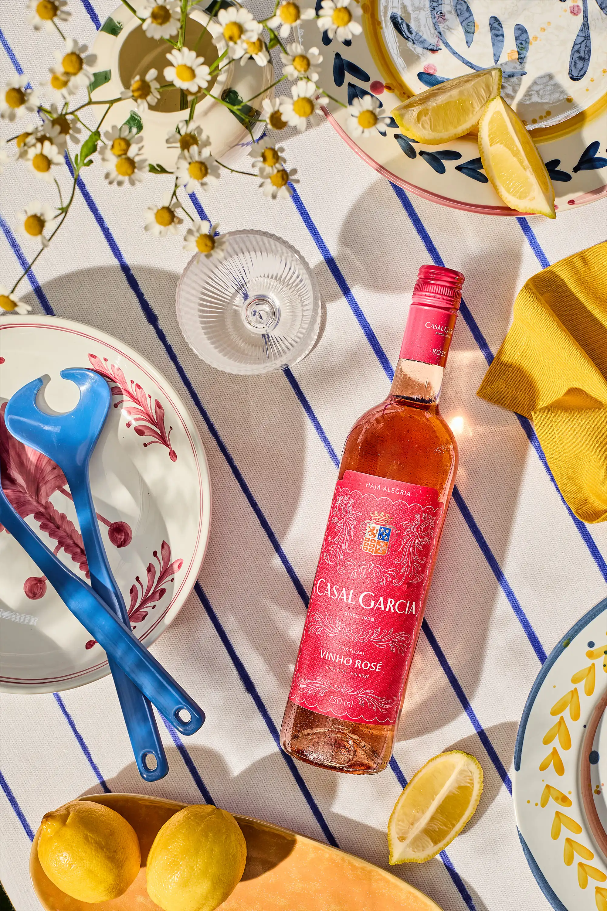 Casal Garcia Vinho Rosé liegend auf sommerlichem Holztisch mit Margeritenblumen, Zitronen und frischem Salat in mediterraner Atmosphäre