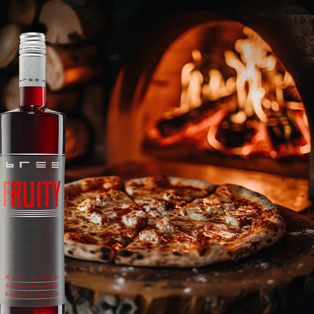 Bree Fruity Rot Weinflasche mit einer frisch gebackenen knusprigen Pizza vor einem traditionellen Pizzaofen als fruchtige Weinbegleitung in gemütlicher Atmosphäre