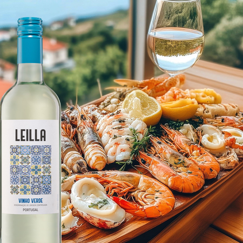 Leilla Vinho Verde mit Meeresfrüchteplatte vor sonniger mediterraner Bucht, sommerliches Genussmotiv