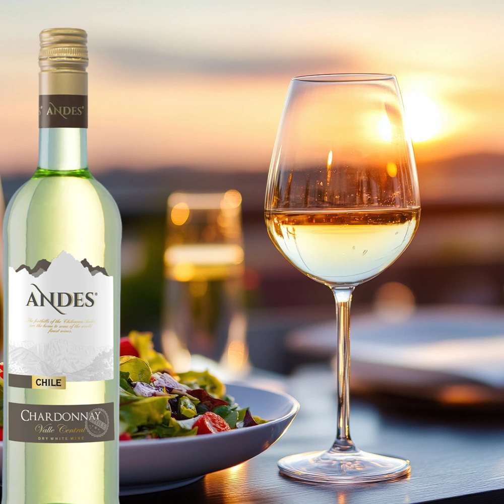 Flasche Andes Chardonnay 0,75 L neben einem Teller frischen Salats und einem Glas Wein auf einem gedeckten Tisch, im Hintergrund die untergehende Sonne