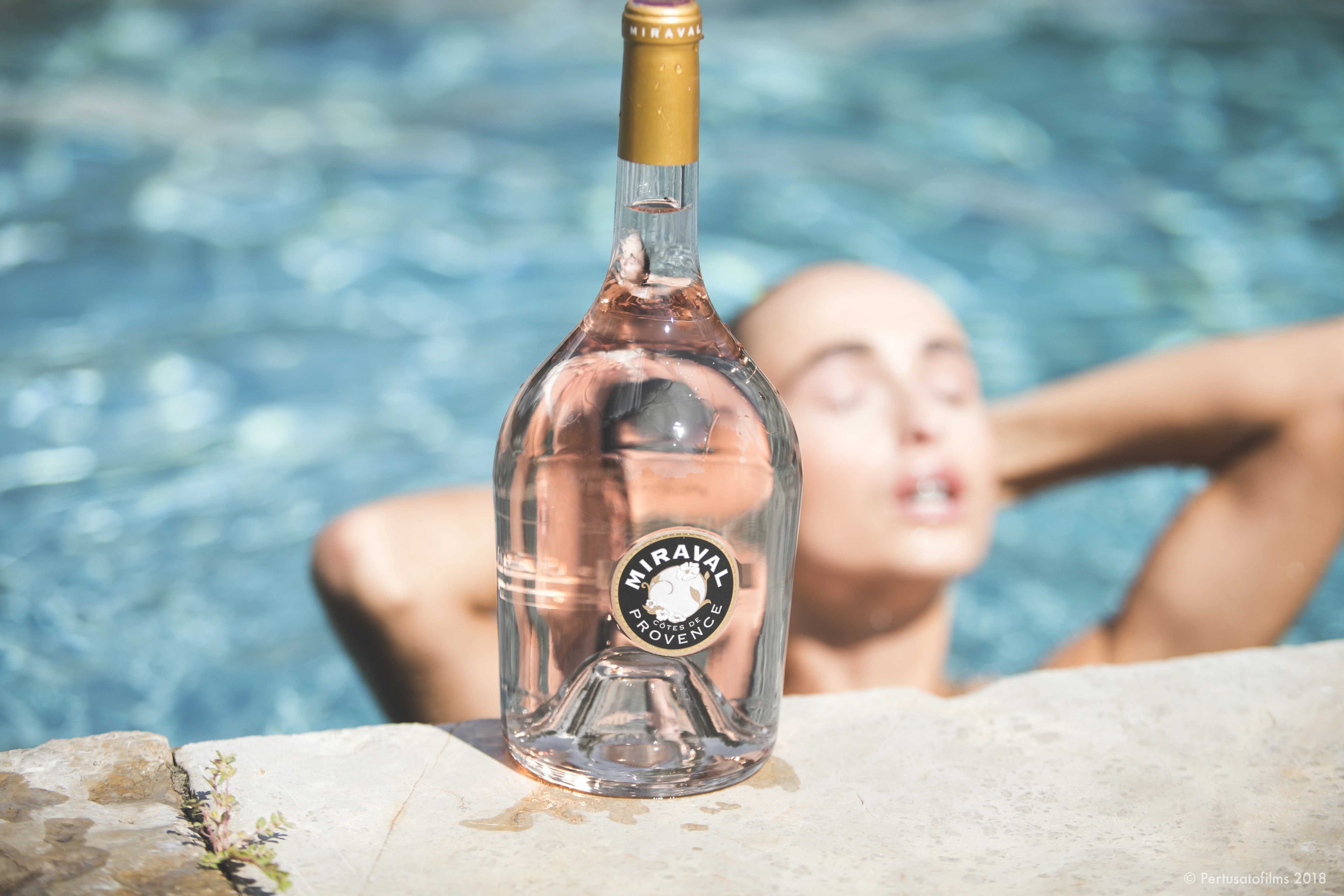 Miraval Rosé am Poolrand mit einer Frau, die im Hintergrund aus dem Wasser auftaucht, sommerliche Atmosphäre