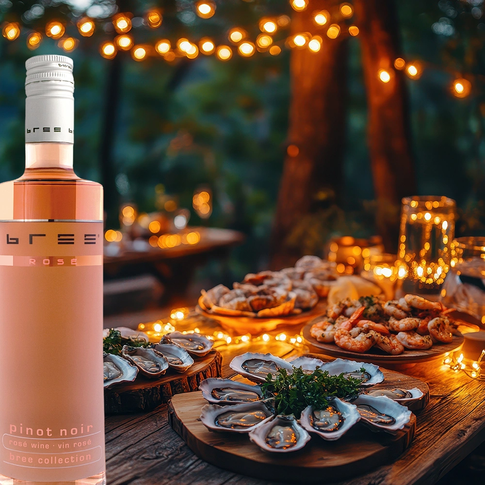 Kleine 0,25-Liter-Flasche Bree Pinot Noir Rosé auf einem rustikalen Holztisch mit frischen Austern, Meeresfrüchten und stimmungsvoller malerischer Beleuchtung als elegante Weinbegleitung